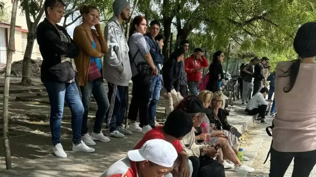 Juicio a creadores de El4tico en Holguín moviliza a decenas y expone tensiones políticas A group of people standing and sitting on stone benches under trees, engaging in conversation or using mobile devices.
